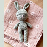 Mint crochet bunny laying on folded pink floral muslin blanket